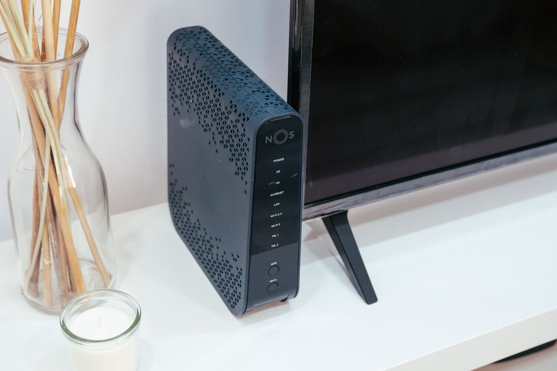 Black home router beside a television and a glass vase.