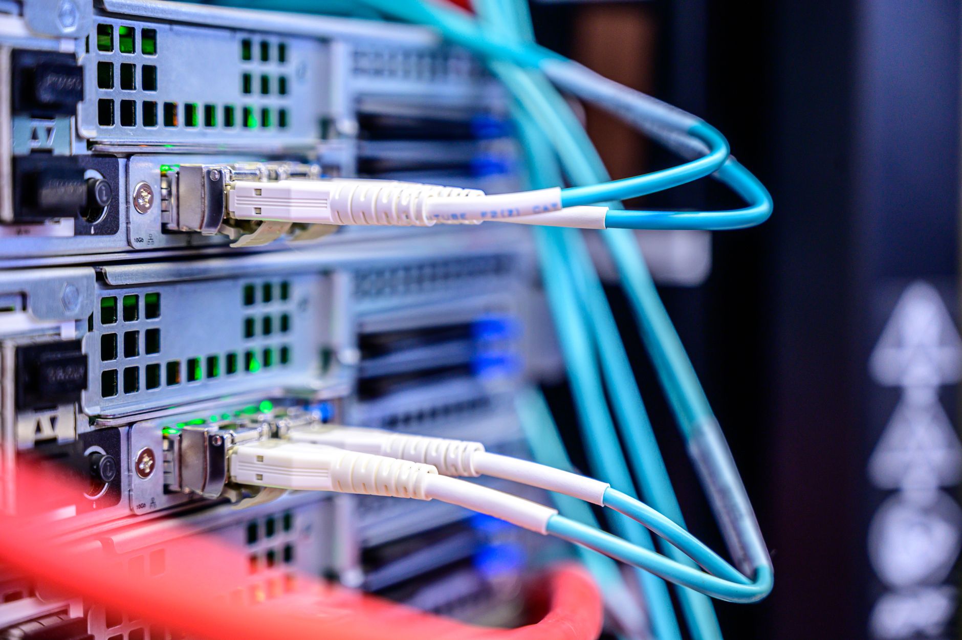 Fiber-optic cables plugged into network transceivers in a server rack.