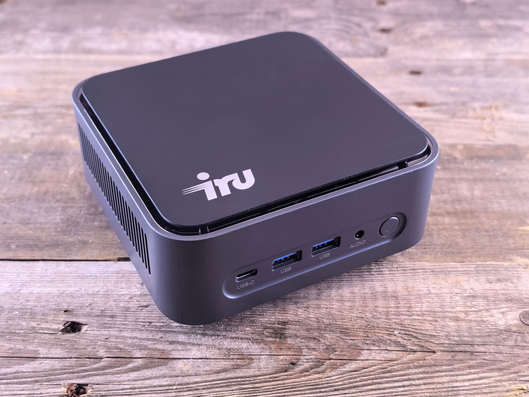 Compact desktop mini PC resting on a wooden table, with front ports visible.